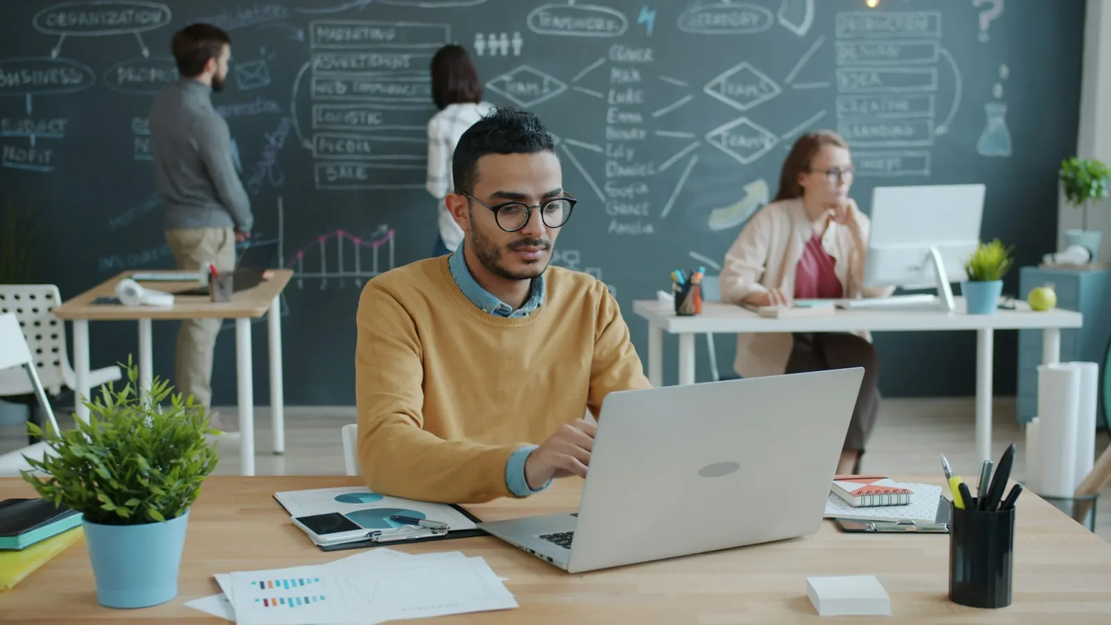 Team working on laptops in a modern office with a planning board behind them